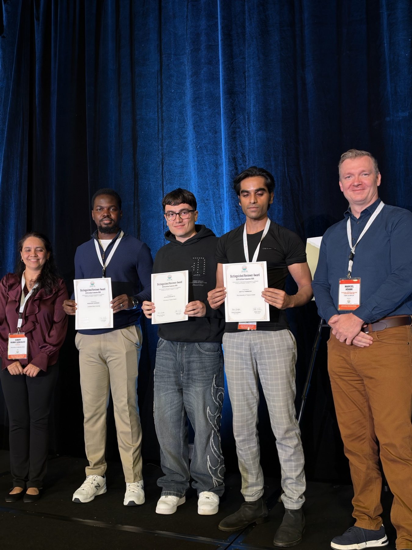 Receiving the Distinguished Reviewer Award on stage at ISSTA 2026, alongside two other awardees and two committee members.